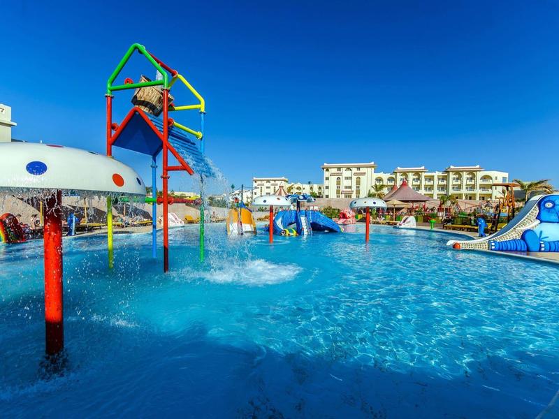Water park with water features and slides in front of a hotel under blue sky.