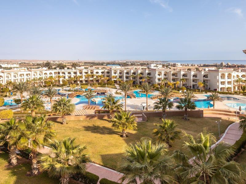 View of a hotel resort with multiple pools, palm trees, and garden areas under a clear sky.
