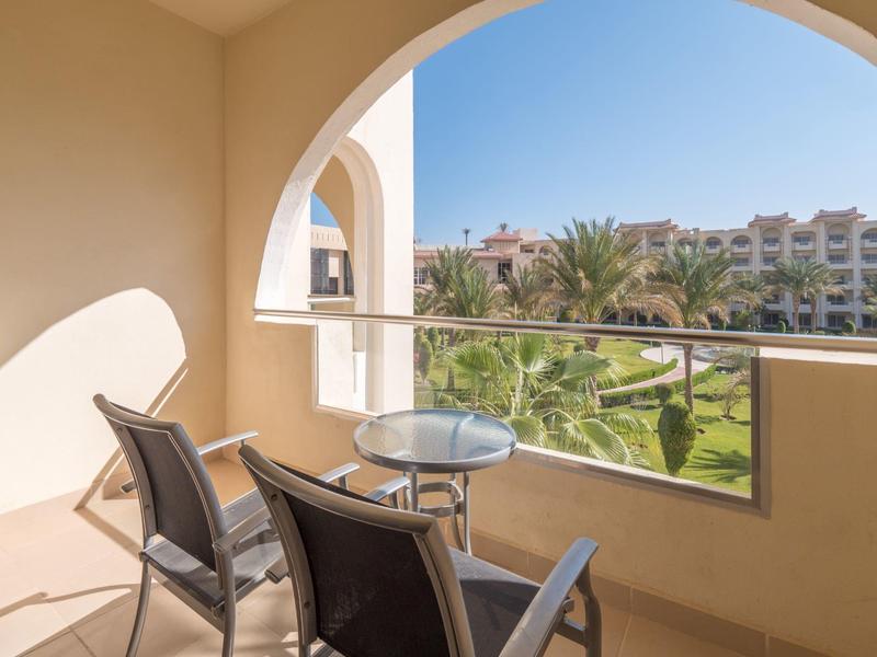 Balcony with two chairs and small table overlooking a garden and buildings.