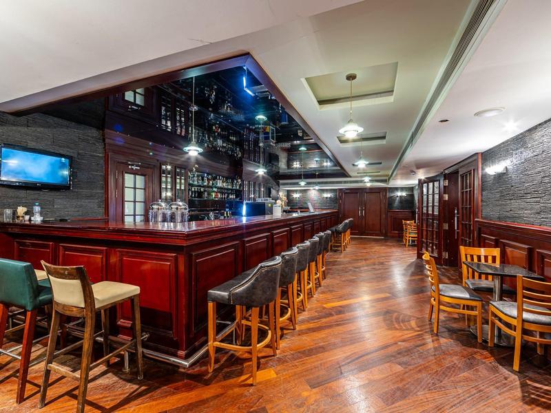 Hotel bar with long wooden counter, stools, and several tables with chairs.