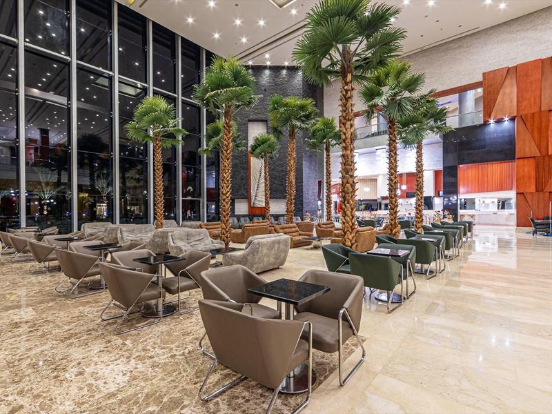 Modern hotel lobby with tall palm trees, comfortable armchairs, and large window area.