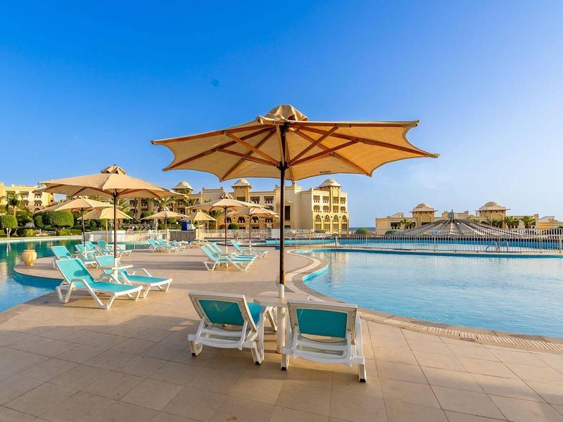 Pool area with two sun loungers under an umbrella and large resorts in the background.