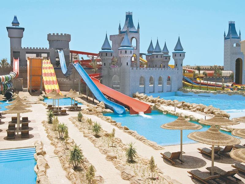Water park with castle-themed slides and pools, surrounded by sunbeds and umbrellas.