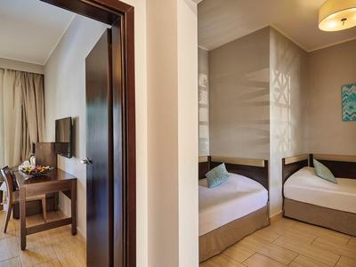 Innenansicht eines Hotelzimmers mit zwei Einzelbetten, Schreibtisch, Fernseher und Balkon im Tageslicht.
