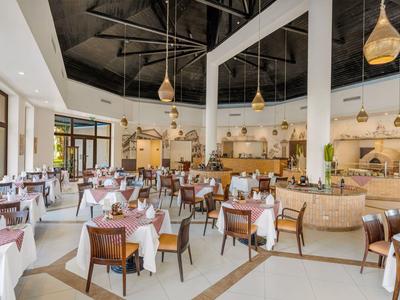 Elegancka sala jadalna hotelu z białymi stołami i drewnianymi krzesłami pod wysokimi sufitami.