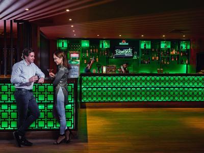 Zwei Personen unterhalten sich an einer bar mit grün leuchtender Theke in stilvollem Ambiente.