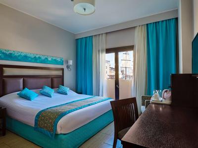 Modernes Hotelzimmer mit Doppelbett, türkisfarbenen Vorhängen und Kissen, Schreibtisch und Balkon.