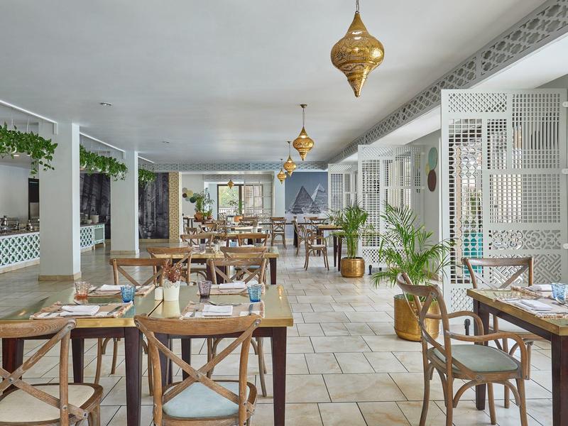 Helles, modernes Restaurant mit Holzstühlen, Tischen, Pflanzen und goldenen Hängelampen.