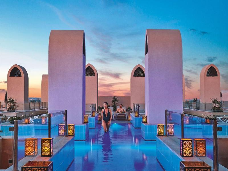 Moderner Pool mit glattem Wasser, dekorativen Laternen und blau-rotem Himmel im Abendlicht.