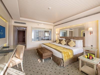 Modern eingerichtetes Hotelzimmer mit großem Bett, TV, Schreibtisch und sitzbarer Couch.