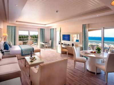 Großes Zimmer mit Holzboden, Doppelbett, Sofa, Esstisch und Meerblick durch große Fenster.