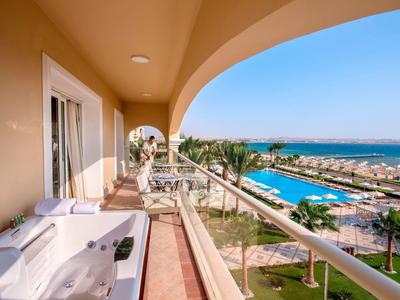 Balkon mit Whirlpool, Glasgeländer und Blick auf Hafen, Meer und blauen Himmel.