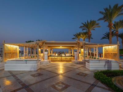 Bar dell'hotel illuminata con aree salotto, circondata da palme al crepuscolo.