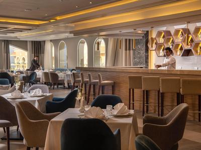 Ristorante elegante con bar con sedute e tavoli apparecchiati in luce calda.