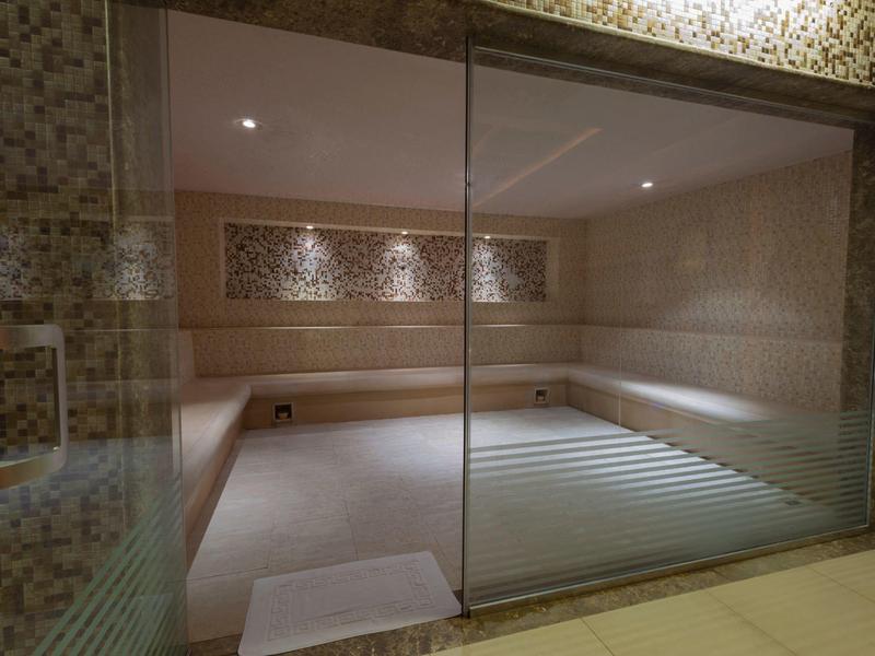 Moderner Saunaraum mit Holzbank, gläserner Tür und warmen, gedämpften Beleuchtungselementen.