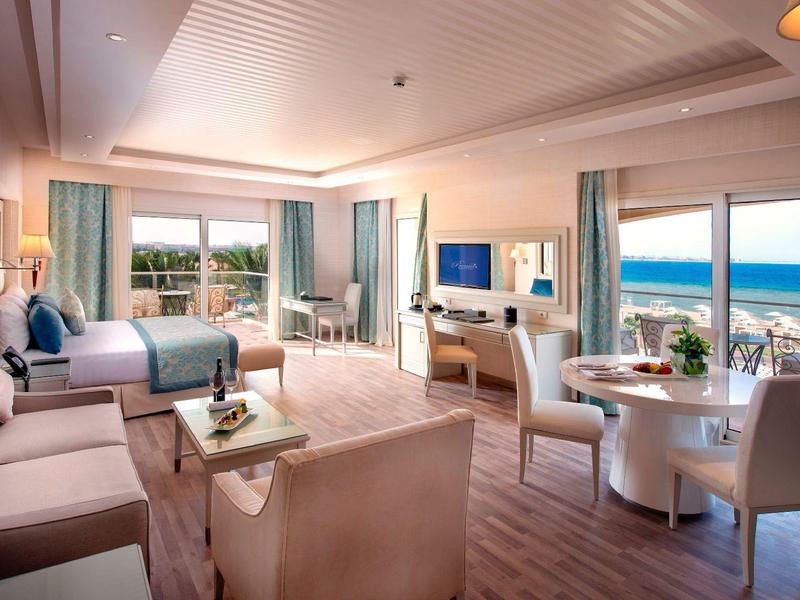 Großes Zimmer mit Holzboden, Doppelbett, Sofa, Esstisch und Meerblick durch große Fenster.