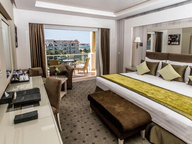 Großes Resort mit Pool, Palmen und Liegestühlen nahe Meer unter klarem Himmel.