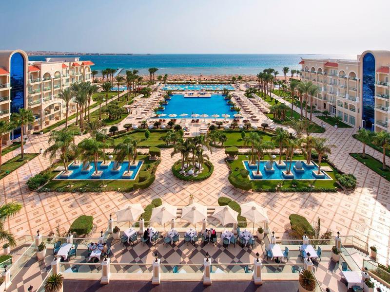 Großes Resort mit Pool, Palmen und Liegestühlen nahe Meer unter klarem Himmel.