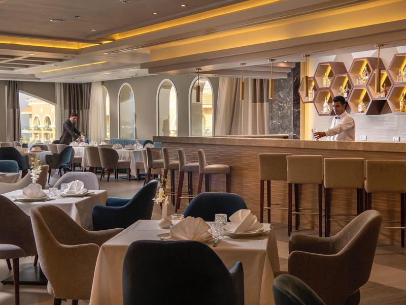 Elegantes Restaurant mit Holztheke, braunen Sesseln, Tischdecken und warmem Deckenlicht.