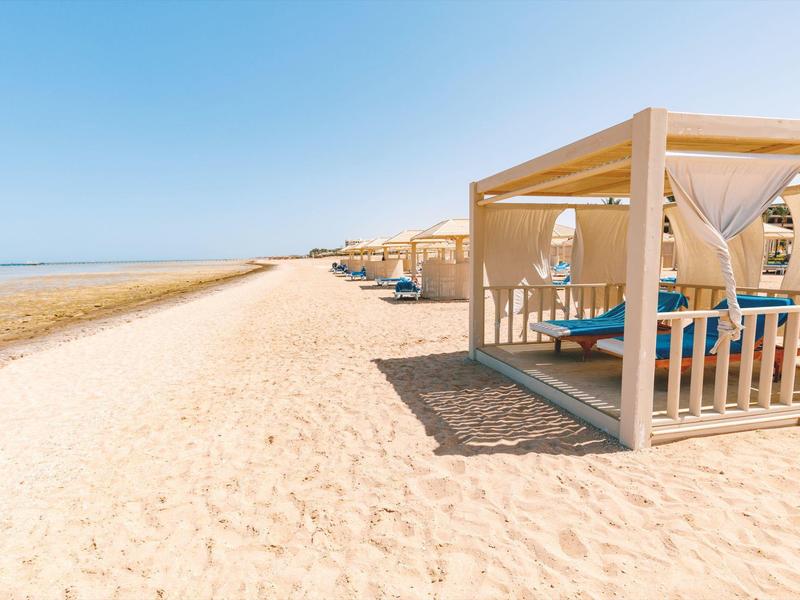 Sandstrand mit weißen Sonnenschutzzelten und klarem blauem Himmel am ruhigen Meer.
