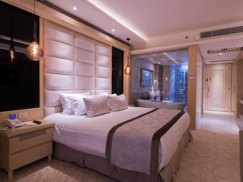 Chambre d'hôtel moderne avec grand lit, tables de chevet et fenêtre panoramique.