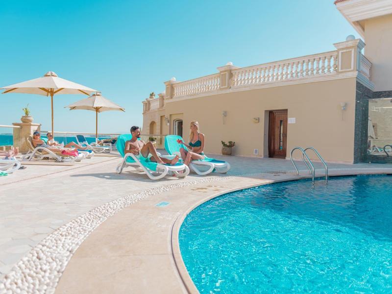 Plusieurs personnes se détendent sur des chaises longues au bord d'une piscine avec vue sur la mer sous un ciel clair.