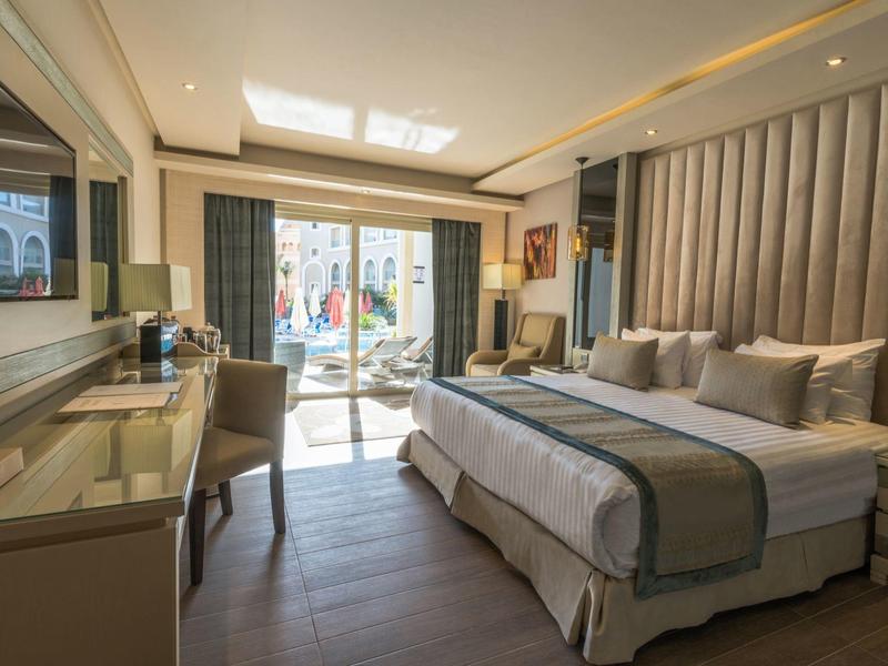 Chambre d'hôtel moderne avec grand lit, bureau et accès au balcon avec coin salon.