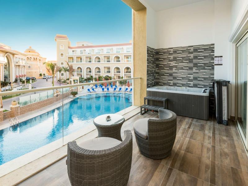 Balcon surplombant la piscine, deux chaises en rotin et une table ronde, jacuzzi moderne sur sol en bois.