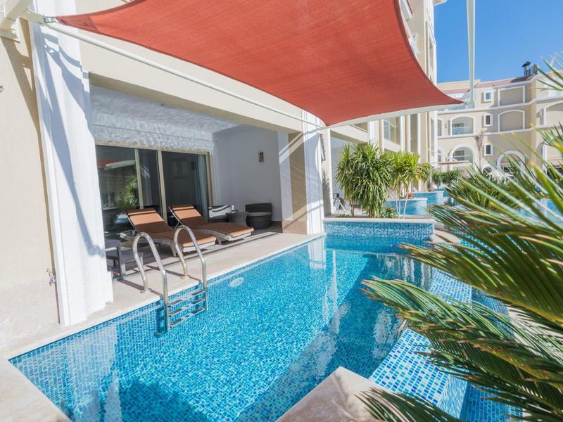 Piscine privée moderne à côté de la terrasse avec sièges et pare-soleil dans un complexe hôtelier.