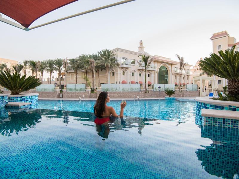 Femme se détend dans la piscine avec un complexe hôtelier exotique en arrière-plan au coucher du soleil.