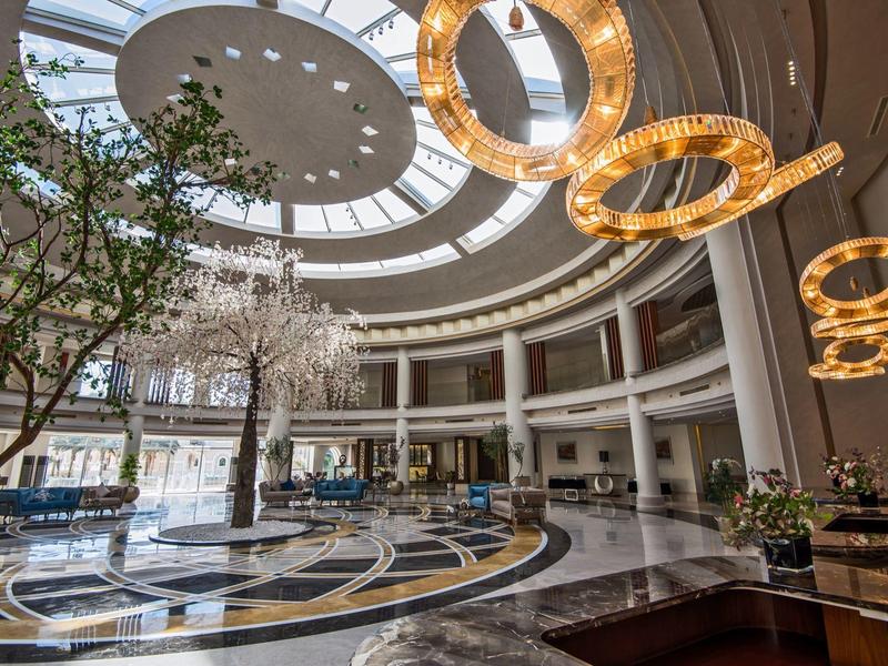 Grand hall d'hôtel avec lustres circulaires, un arbre et un puits de lumière.