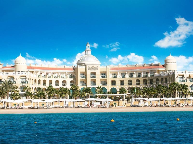 Grand hôtel avec coupoles au bord de l'eau sous un ciel bleu clair.
