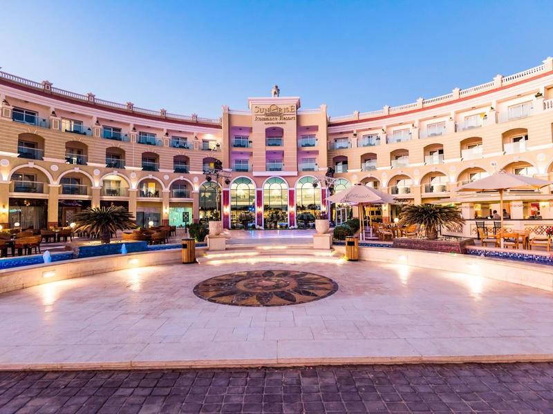 Grand hôtel en demi-cercle avec cour ouverte et fontaine décorative au centre.