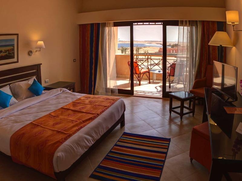 Gemütliches Hotelzimmer mit Doppelbett, buntem Teppich, Schreibtisch, Balkon und Blick aufs Meer.