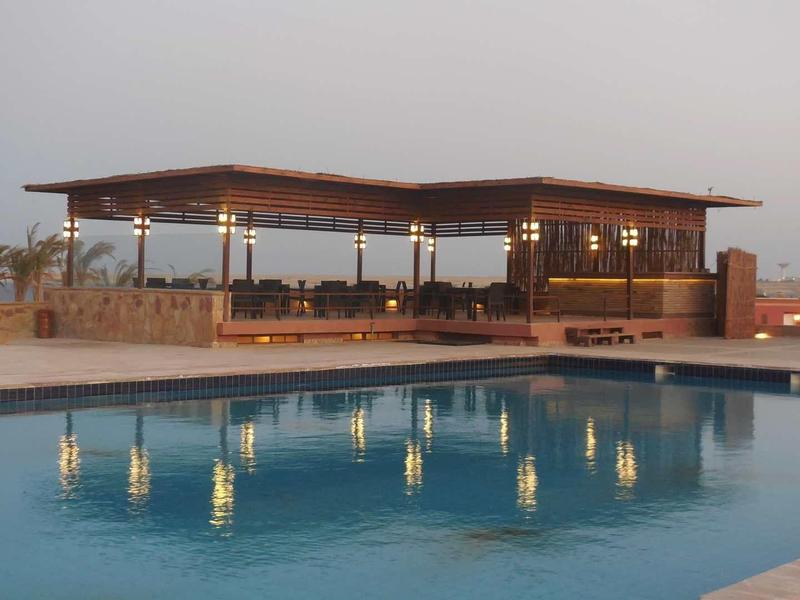 Ein Schwimmbecken mit klar blauem Wasser vor offenem, überdachtem Terrassenbereich bei Sonnenuntergang.