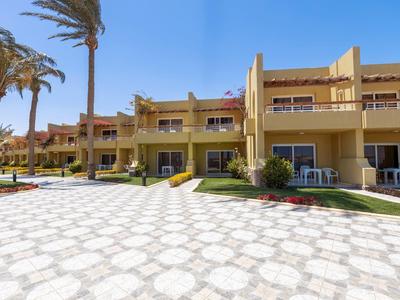 Řady žlutých dvoupodlažních rekreačních apartmánů s venkovními prostory a palmami za slunečného počasí.