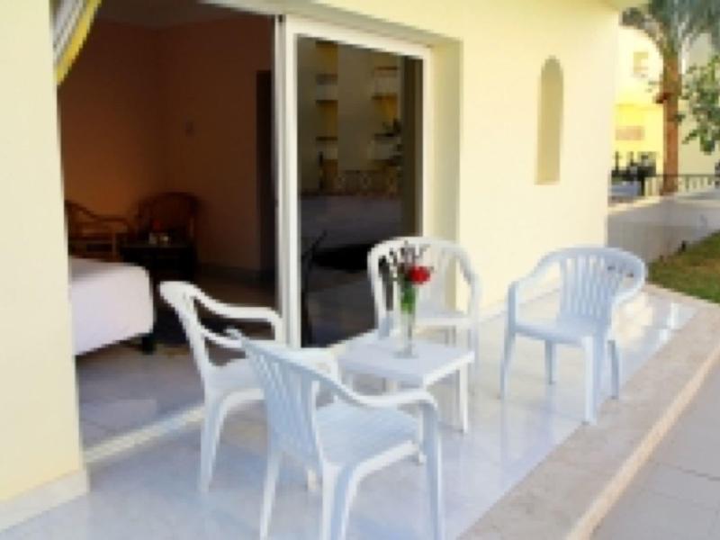 Kleiner Balkon mit weißem Kunststofftisch und Stühlen vor einem gelben Haus mit Schiebetür.