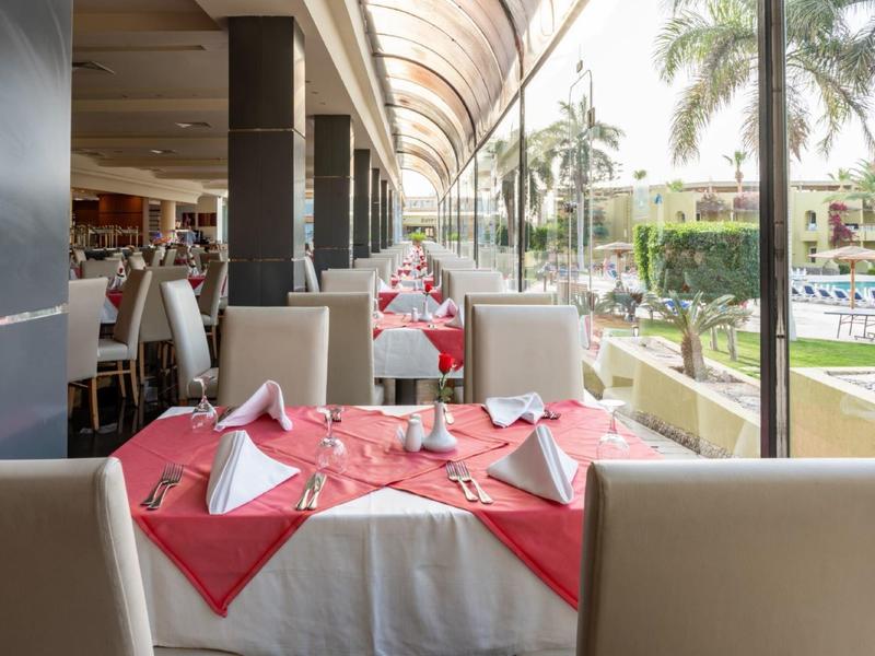 Hotelová restaurace s prostřeným stolem a výhledem na bazén a palmy.