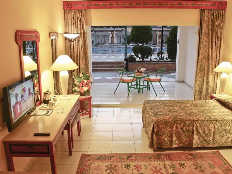 Helles Schlafzimmer mit Doppelbett, Fernseher, Schreibtisch und Terrasse mit Blick nach draußen.