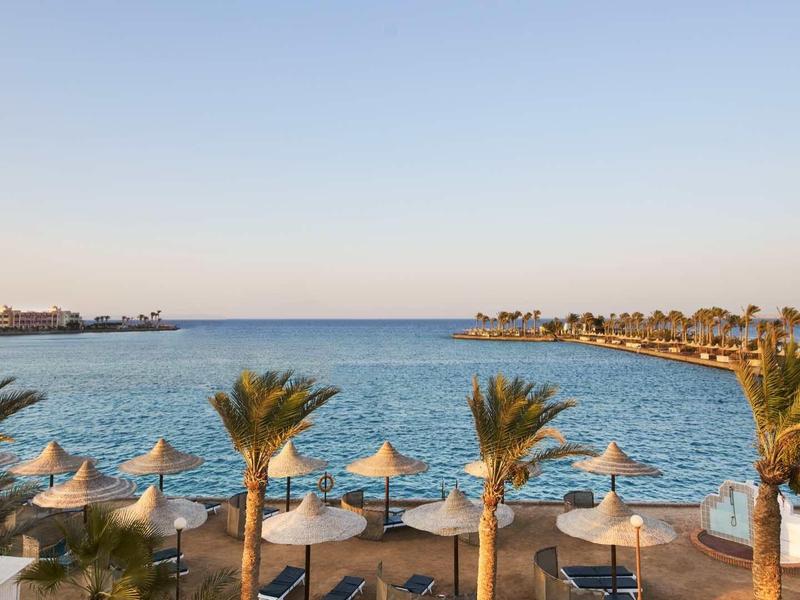 Strand mit Palmen, Sonnenschirmen und blauem Meer unter klarem Himmel im Abendlicht.