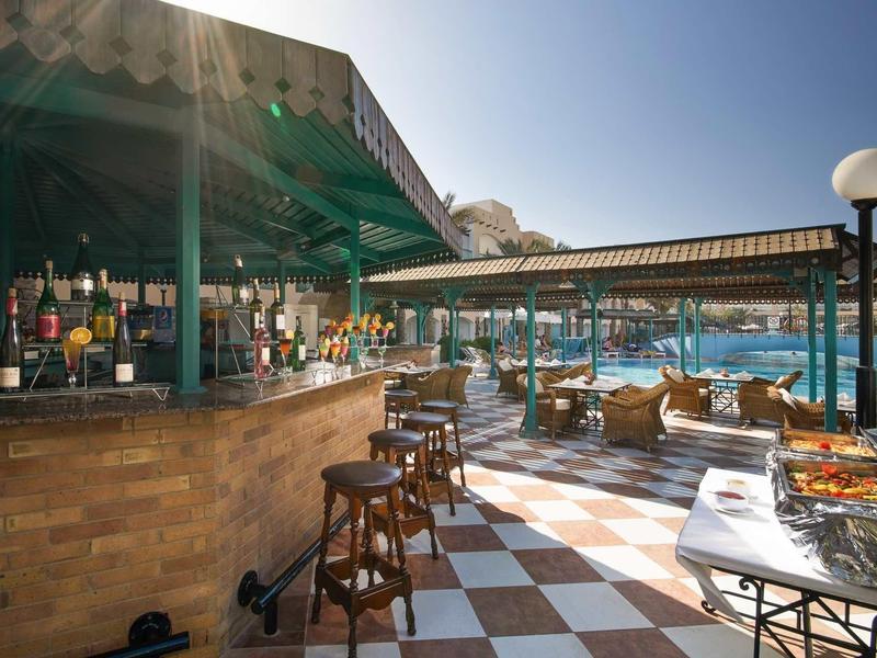 Offene Strandbar mit Holzstühlen, Theke, Sonnenschirmen und Blick auf das Meer bei Sonnenschein.