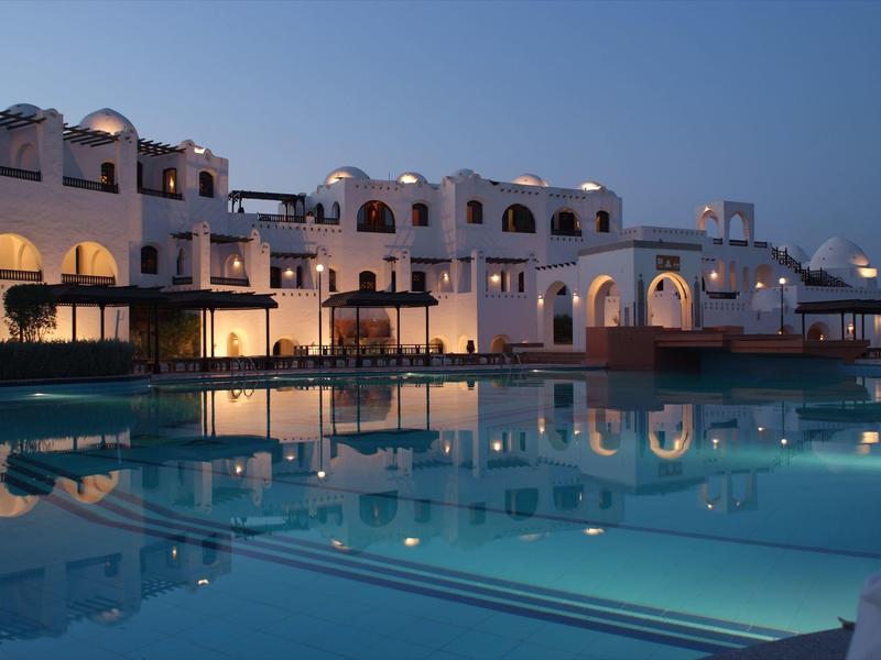 Beleuchtetes Hotelgebäude mit Pool bei Nacht, ruhige und elegante Atmosphäre.