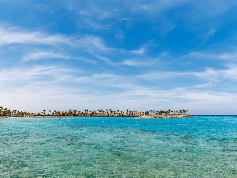Panoramablick auf eine Küste mit klarem, blauem Wasser und bewölktem Himmel.