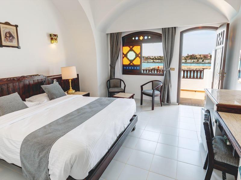 Helles Hotelzimmer mit großem Bett, Balkon und Blick aufs Wasser.