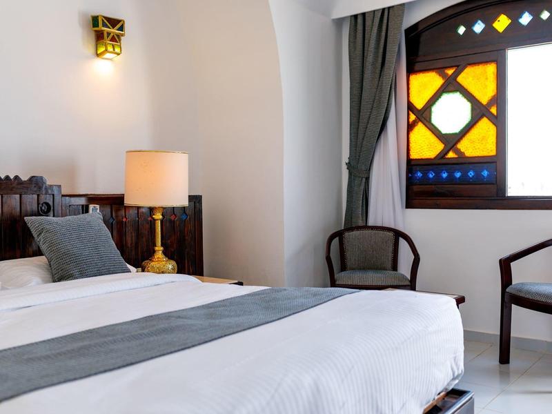 Helles Hotelzimmer mit Doppelbett, modernem Lampenlicht und farbigem Fenster.