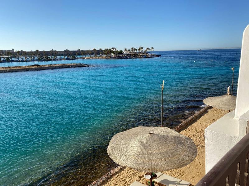 Klares blaues Wasser und Strand mit Sonnenschirm am Meer vom Balkon aus gesehen.