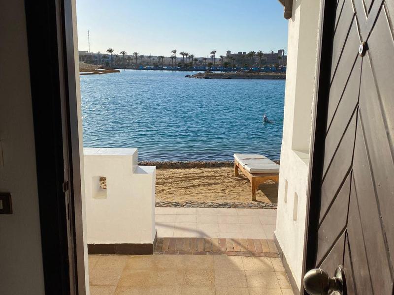 Blick durch eine geöffnete Tür auf eine Terrasse und Meer mit klarem Himmel.