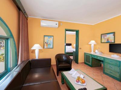 Helles Hotelzimmer mit braunem Sofa, Sessel, TV und Blick auf Innenhof.