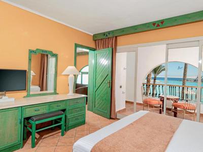 Hell eingerichtetes Hotelzimmer mit grünem Mobiliar und Balkon mit Meerblick.