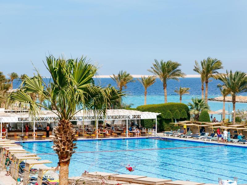 Großer Pool mit Palmen und Meerblick in einem sonnigen Resort.